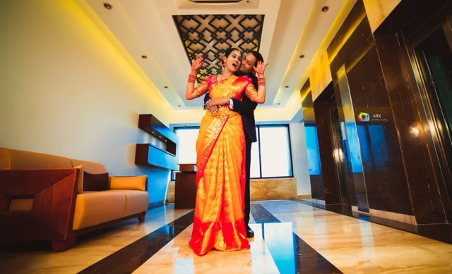 Bride in a red and gold silk saree standing in a modern hallway