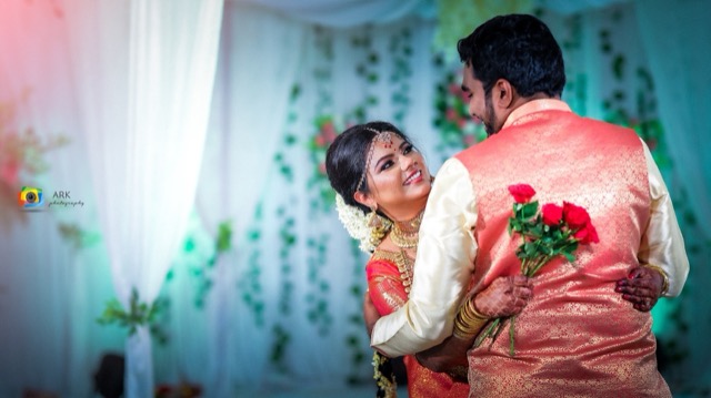 Couple sharing a moment in front of a floral backdrop, holding roses
