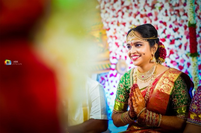 Bride in a green silk saree with folded hands before a floral backdrop