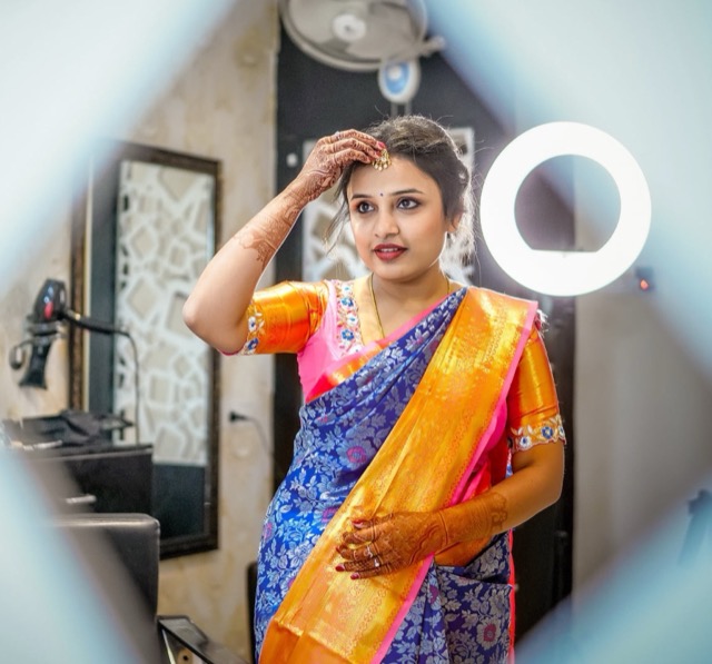 Woman in a blue and gold saree adjusting her hair in a ring-light mirror