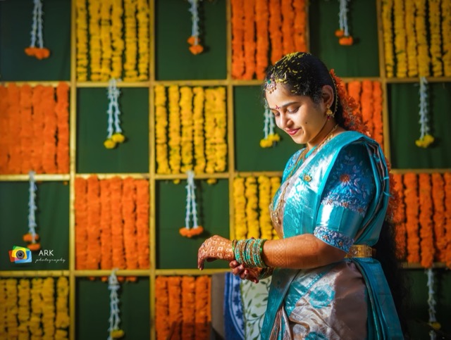 Young woman in a blue half-saree in front of a marigold flower wall