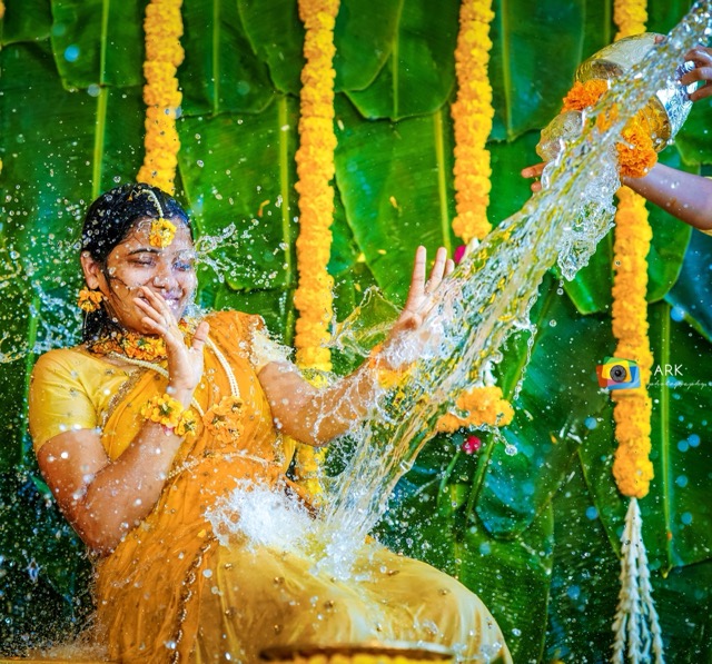 Bride in yellow laughing as water is poured during the mangala snanam ritual