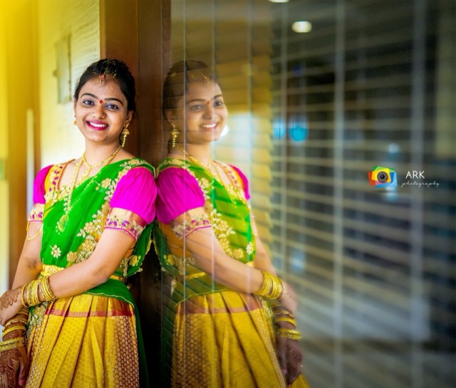 Girl in a green and yellow half-saree with her reflection in glass