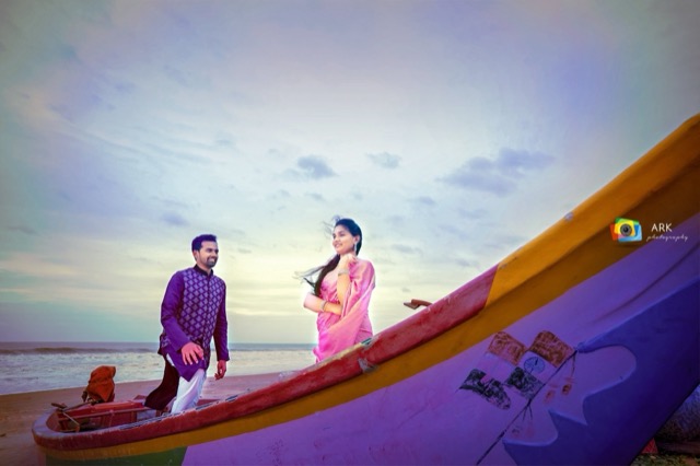 Couple on the beach beside a colourful fishing boat at dusk